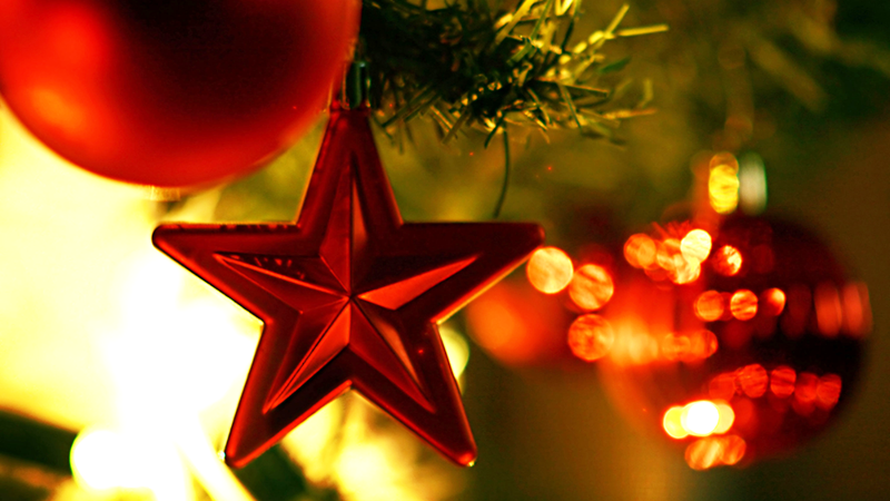 A close-up of a red star hanging on a festively decorated Christmas tree.