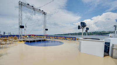 Une des terrasses extérieures du navire AML Cavalier Maxim. Des tables et des chaises sont installées. Vue sur la ville de Lévis en arrière plan