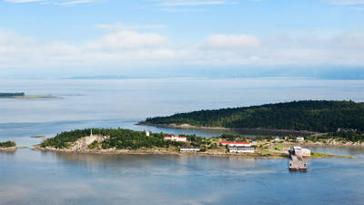 Vue aérienne de Grosse-Île et du fleuve Saint-Laurent. On peut y voir de la verdure et des bâtiments typiques de l'île.