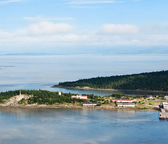 Vue aérienne de Grosse-Île et du fleuve Saint-Laurent. On peut y voir de la verdure et des bâtiments typiques de l'île.