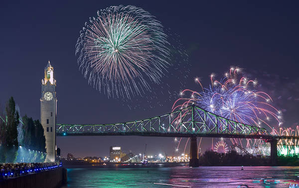 Une vue nocturne spectaculaire d'un feu d'artifice illuminant le ciel au-dessus d'un pont emblématique et d'une tour horloge, avec des lumières urbaines scintillantes et une rivière calme au premier plan.