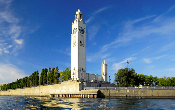 View of the Clock Tower in the Old Port of Montreal from the St. Lawrence River, under a blue sky with a few clouds.