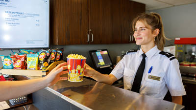 A smiling waitress serving popcorn to a customer. Bistro on board the AML Louis Jolliet in Quebec City