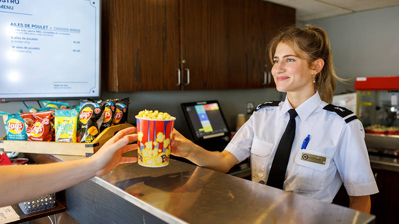 Une serveuse souriante servant du popcorn à un client. Bistro à bord du AML Louis Jolliet à Québec.