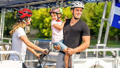 Un couple et un enfant profite d'une balade en navette fluviale sur le Saint-Laurent à Montréal. La femme tient un vélo et porte un casque sur la tête,  l'homme porte l'enfant dans ses bras.