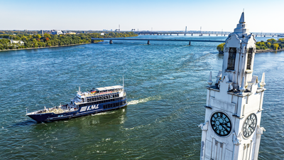 The AML Cavalier Maxim ship sailing on the Saint Lawrence River with the Montreal Clock Tower in the foreground and the Saint Helen's Island and the Samuel de Champlain Bridge in the background