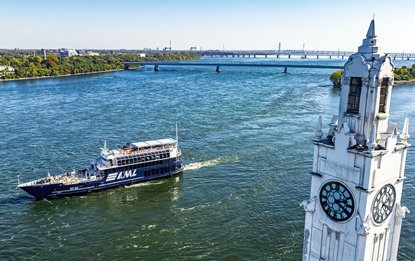 The AML Cavalier Maxim ship sailing on the Saint Lawrence River with the Montreal Clock Tower in the foreground and the Saint Helen's Island and the Samuel de Champlain Bridge in the background