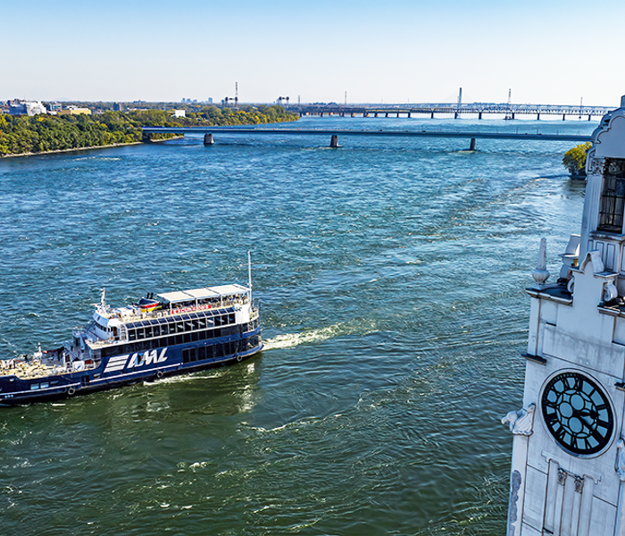 The AML Cavalier Maxim ship sailing on the Saint Lawrence River with the Montreal Clock Tower in the foreground and the Saint Helen's Island and the Samuel de Champlain Bridge in the background