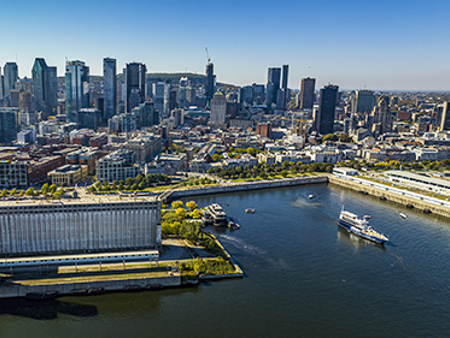 Vue aérienne du navire AML Cavalier Maxim sortant du Vieux Port de Montréal avec une vue sur la ville en arrière plan sous un ciel bleu