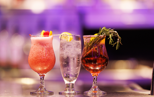  Three cocktails of various colors and garnishes on a bar counter, with a slightly blurred background highlighting the vibrant drinks.