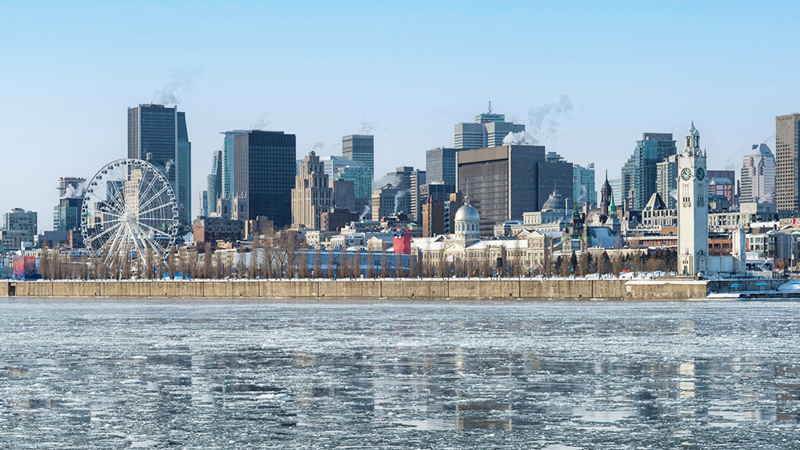 Winter landscape of the Old Port of Montreal with a view of the ferris wheel, the frozen St. Lawrence River in the foreground, and the city skyline in the background.