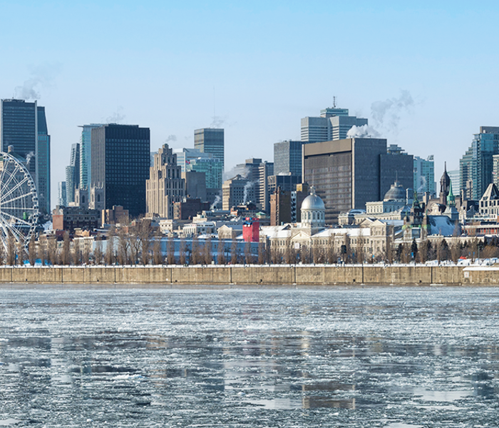 Winter landscape of the Old Port of Montreal with a view of the ferris wheel, the frozen St. Lawrence River in the foreground, and the city skyline in the background.