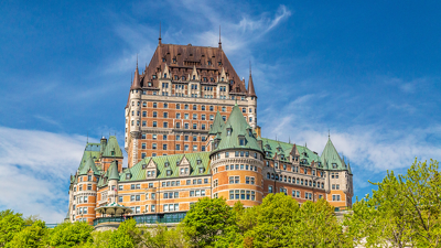  The Château Frontenac in Quebec City standing majestically against a blue sky and lush greenery.