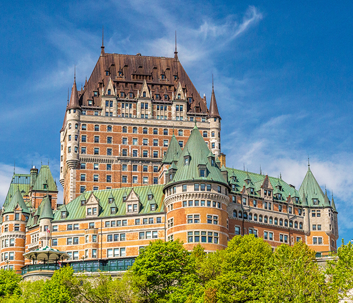  The Château Frontenac in Quebec City standing majestically against a blue sky and lush greenery.