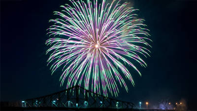 Un feu d'artifice coloré, avec des teintes de vert et de violet, éclate dans le ciel nocturne au-dessus d'un pont emblématique, créant une vue spectaculaire.