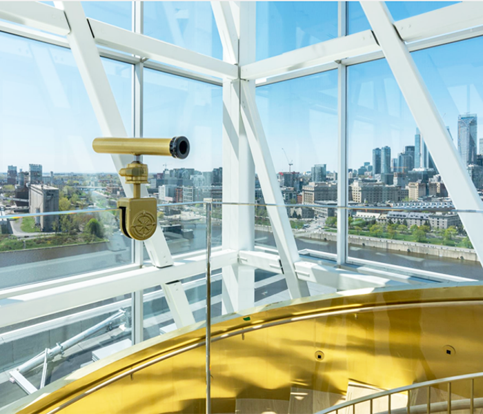 A telescope in a modern observatory with panoramic windows overlooking the Montreal skyline under a blue sky.