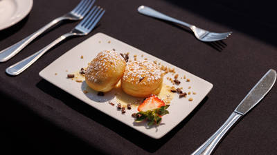 Une assiette de desserts gourmands, composée de deux beignets saupoudrés de sucre glace, garnis de sauce et décorés avec une fraise et des éclats de chocolat.