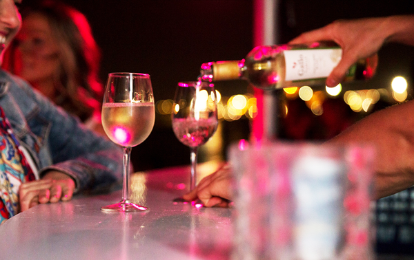 Une femme au bar en train de faire servir un succulent verre de vin blanc frais.