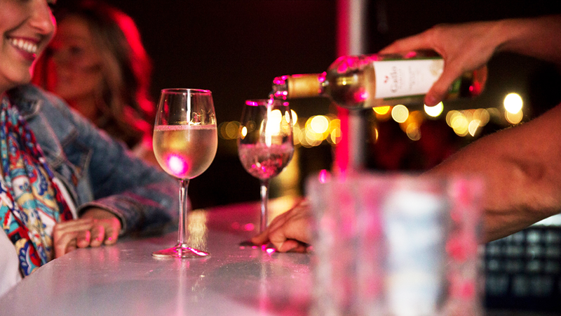 Une femme au bar en train de faire servir un succulent verre de vin blanc frais.