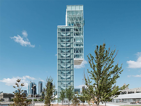 Montreal Port Tower with a tree-lined esplanade in the foreground and Montreal buildings in the background