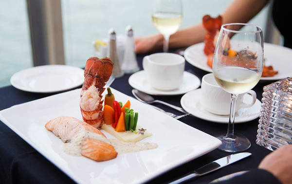 A gourmet dish featuring a salmon fillet, a lobster tail, and fresh market vegetables arranged in an elegant plate.