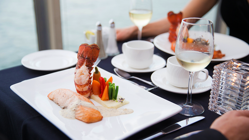 A gourmet dish featuring a salmon fillet, a lobster tail, and fresh market vegetables arranged in an elegant plate.