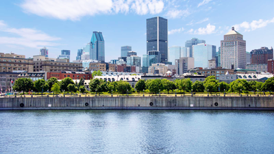 L'horizon de la ville de Montréal avec des bâtiments modernes sous un ciel bleu, avec le fleuve Saint-Laurent au premier plan.