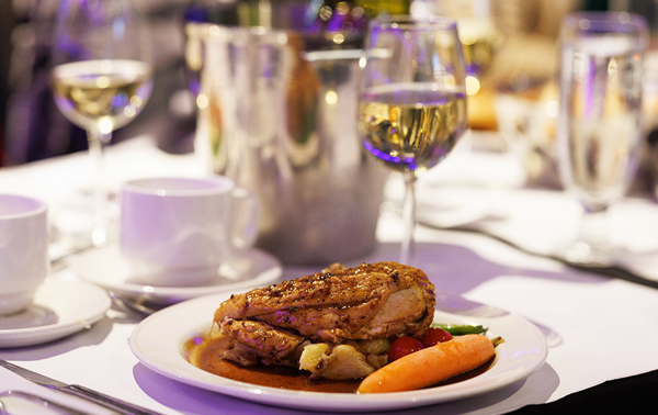 A bistro-style plate featuring a chicken supreme, baby potatoes, and fresh market vegetables, accompanied by a glass of white wine.