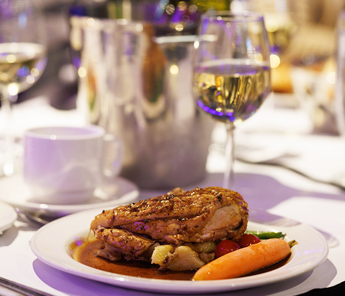 Une assiette bistronomique comprenant un suprême de volaille manchon, des pommes de terre grelots et des légumes frais du marché accompagné d'un verre de vin blanc.