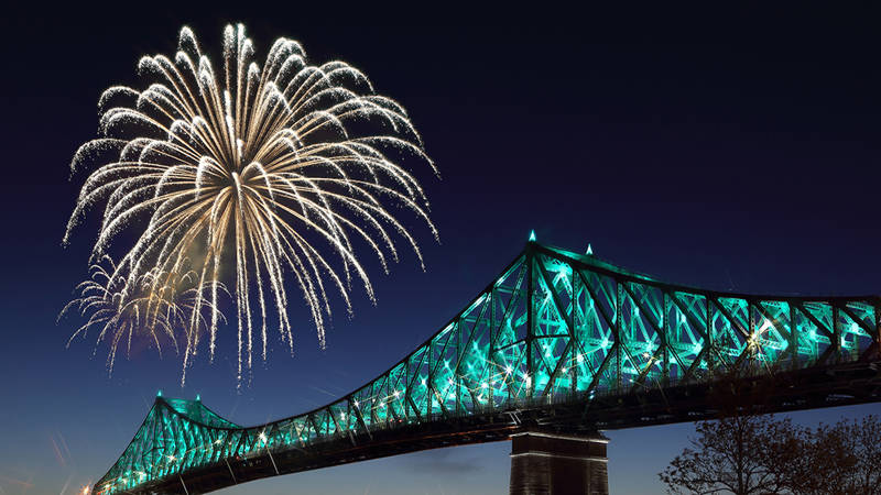 Un feu d'artifice doré illumine le ciel nocturne à côté d'un pont emblématique éclairé avec des lumières turquoise, créant une scène festive et spectaculaire.