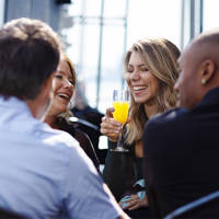 A group of four friends sharing a joyful moment in a restaurant near the water, with a smiling woman holding a glass of mimosa.