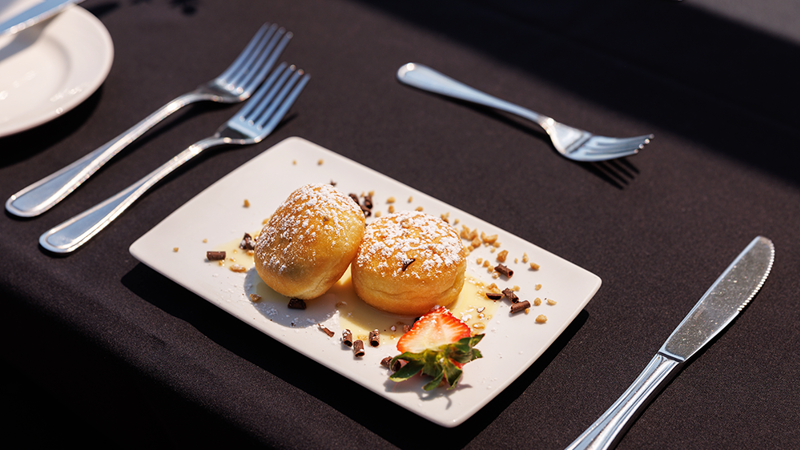  Mini stuffed donuts sprinkled with powdered sugar, beautifully presented on a plate with a fresh strawberry slice and chocolate shavings as decoration.