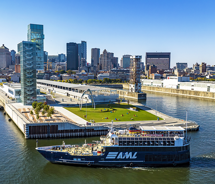 Aerial view of the AML Cavalier Maxim parked in front of the Port of Montreal Tower by day, with a view of the city's sunny skyline in the background.