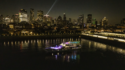 Vue aérienne du navire AML Cavalier Maxim stationné dans le Vieux-Port de Montréal de nuit avec vue sur la skyline de la ville en arrière plan.