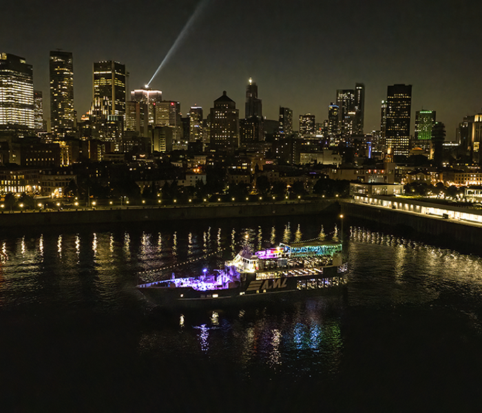 Vue aérienne du navire AML Cavalier Maxim stationné dans le Vieux-Port de Montréal de nuit avec vue sur la skyline de la ville en arrière plan.