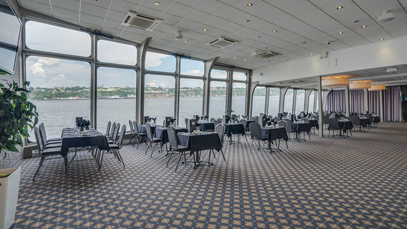 Indoor room with set tables and large bay windows overlooking the Saint Lawrence River in Quebec City