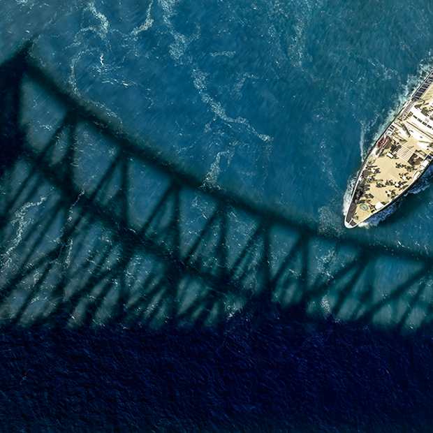 Aerial view of the Cavalier Maxime sailing on the sparkling St. Lawrence River, with the shadow of the Jacques Cartier Bridge in the foreground.