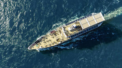 Vue aérienne d'un bateau de croisière naviguant sur des eaux bleues, avec des passagers sur le pont profitant du voyage.