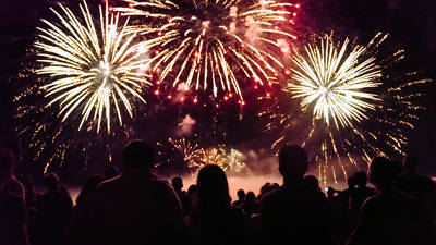 Une foule admire un spectaculaire feu d'artifice illuminant le ciel nocturne avec des éclats dorés et rouges, créant une ambiance festive et magique.