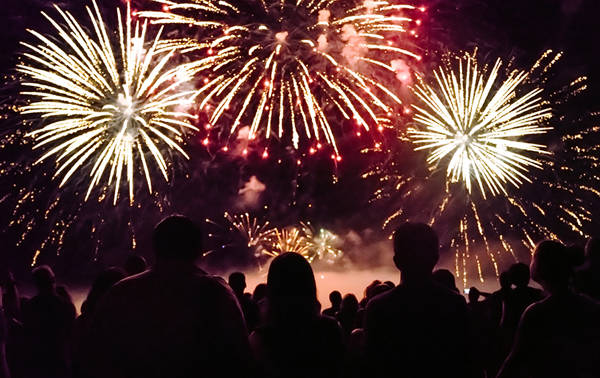 Une foule admire un spectaculaire feu d'artifice illuminant le ciel nocturne avec des éclats dorés et rouges, créant une ambiance festive et magique.