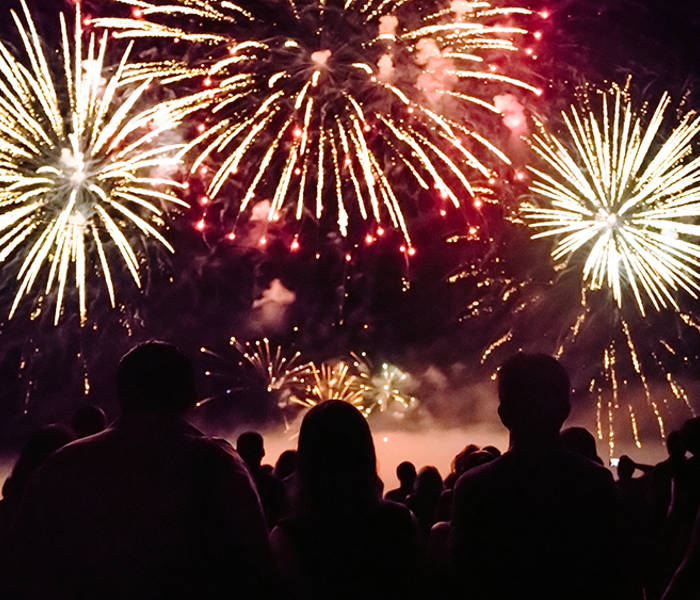 Une foule admire un spectaculaire feu d'artifice illuminant le ciel nocturne avec des éclats dorés et rouges, créant une ambiance festive et magique.