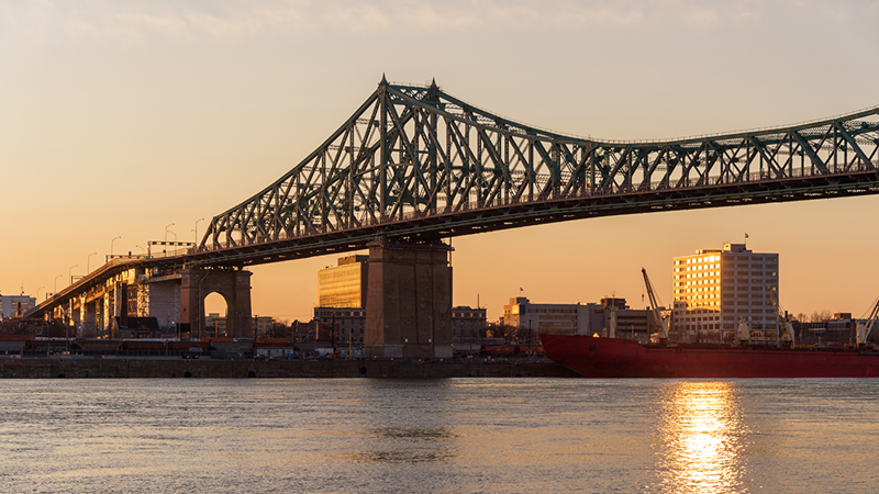 Le Pont Jacques Cartier entouré de la lumière chaleureuse d'un coucher de soleil qui apparait en arrière plan.