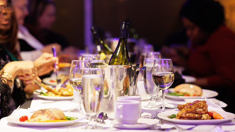 A close-up of a dinner cruise table set with dishes, glasses, and bottles of champagne and wine.