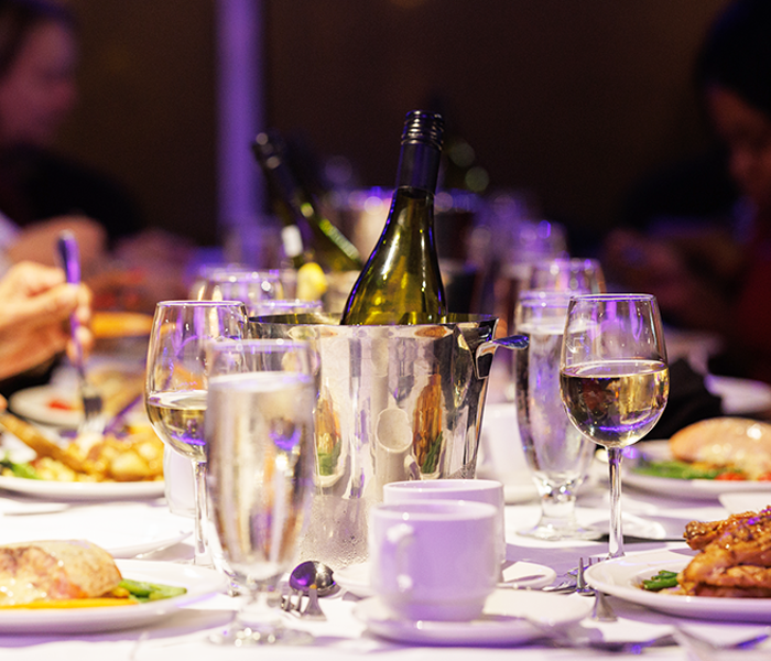 A close-up of a dinner cruise table set with dishes, glasses, and bottles of champagne and wine.