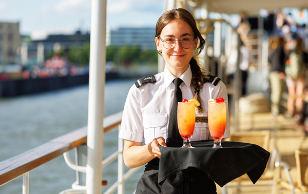 A waitress holding a tray with orange cocktails on the outdoor terrace of the AML Cavalier Maxim ship in Montreal.