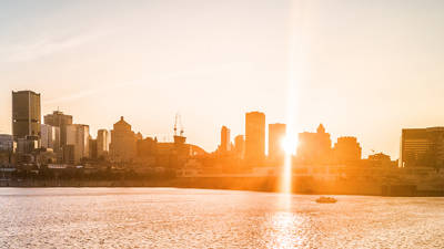 Une silhouette urbaine baignée dans une lumière dorée au coucher du soleil, avec des gratte-ciels en arrière-plan et une rivière scintillante au premier plan.