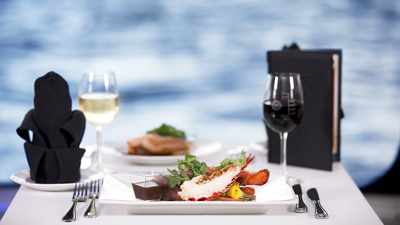 A plate of lobster, a glass of white wine, and red wine on a table overlooking the St. Lawrence River in Montreal.