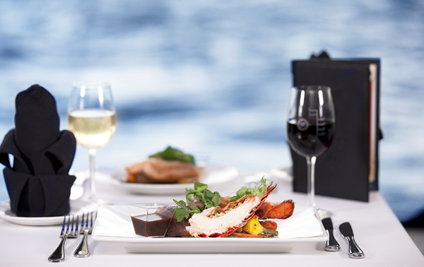 A plate of lobster, a glass of white wine, and red wine on a table overlooking the St. Lawrence River in Montreal.