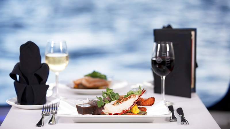 A plate of lobster, a glass of white wine, and red wine on a table overlooking the St. Lawrence River in Montreal.