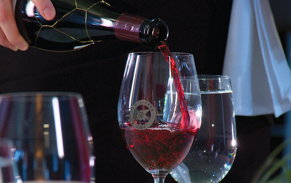 A close-up of a waiter pouring red wine into a glass.